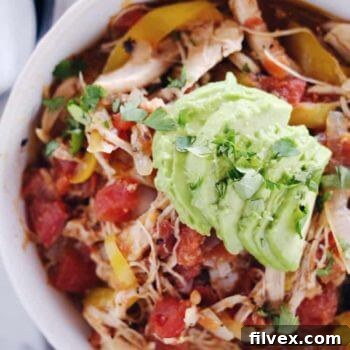 Crockpot chicken enchilada soup in a bowl with sliced avocado and onions on top
