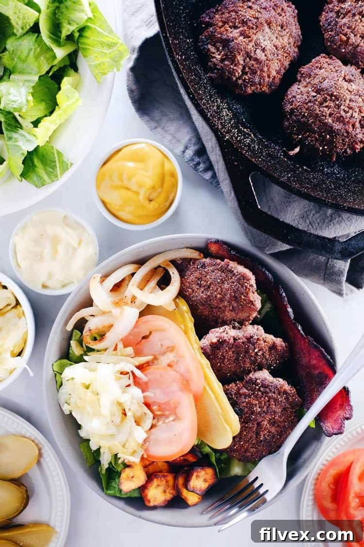 A vibrant Mini Burger Bowl featuring mini beef patties, fresh greens, crispy fried plantains, tangy sauerkraut, sliced tomatoes, red onion, and crumbled bacon.