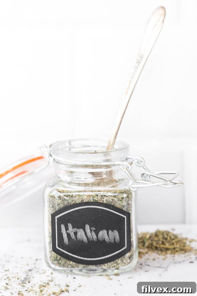 Italian seasoning blend in a labeled glass jar, with a small wooden spoon emerging from the top, suggesting its use.