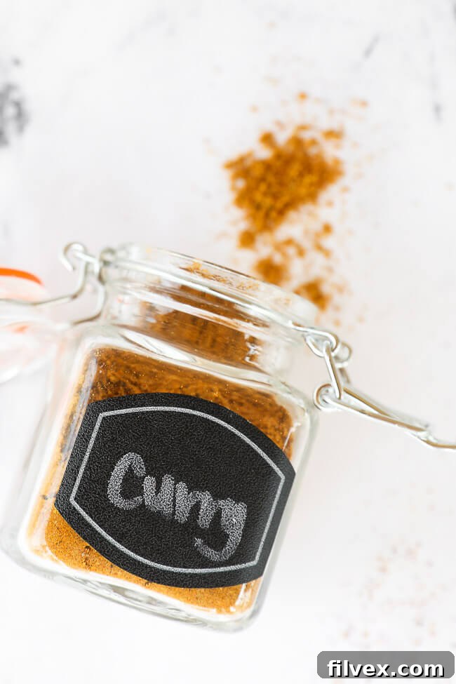 Curry seasoning mix in a labeled glass jar, lying on its side with a small amount of spice gently spilling from the top.