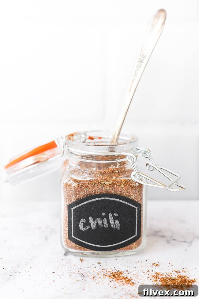 Chili seasoning in a labeled glass jar, with a small wooden spoon gently scooping out some of the blend.