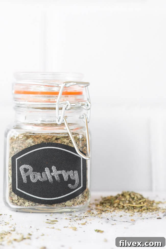 Poultry seasoning in a labeled glass jar, with a small amount of the blend sprinkled around the base of the jar on a textured surface.