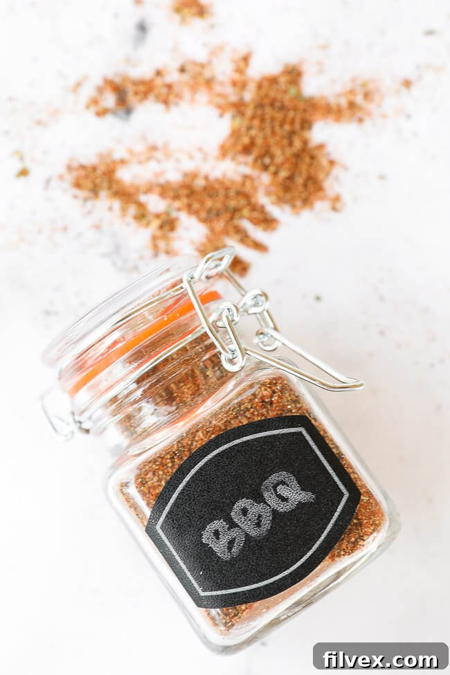 BBQ seasoning in a labeled glass jar, lying on its side on a countertop with scattered spices, creating an appealing visual.