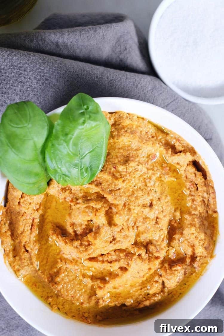 Scooping rich garlic basil nut hummus from a bowl, highlighting its thick and smooth texture, an excellent legume-free dip for various snacks.