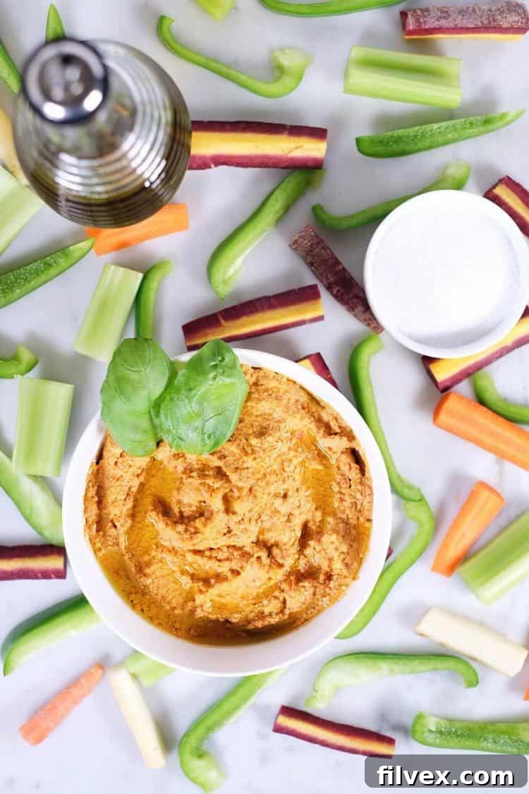 A bowl of fresh garlic basil nut hummus, surrounded by colorful vegetable sticks and plantain chips, ready for a healthy snack or party spread.