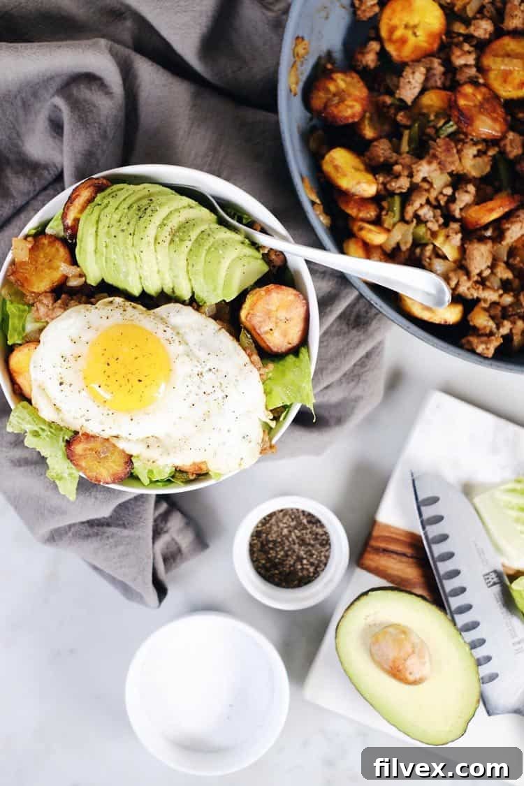 Baked ripe plantain slices, golden brown and caramelized, glistening on a baking sheet. These tender, sweet plantains are a key component of the healthy and flavorful Pork and Plantain Bowl.