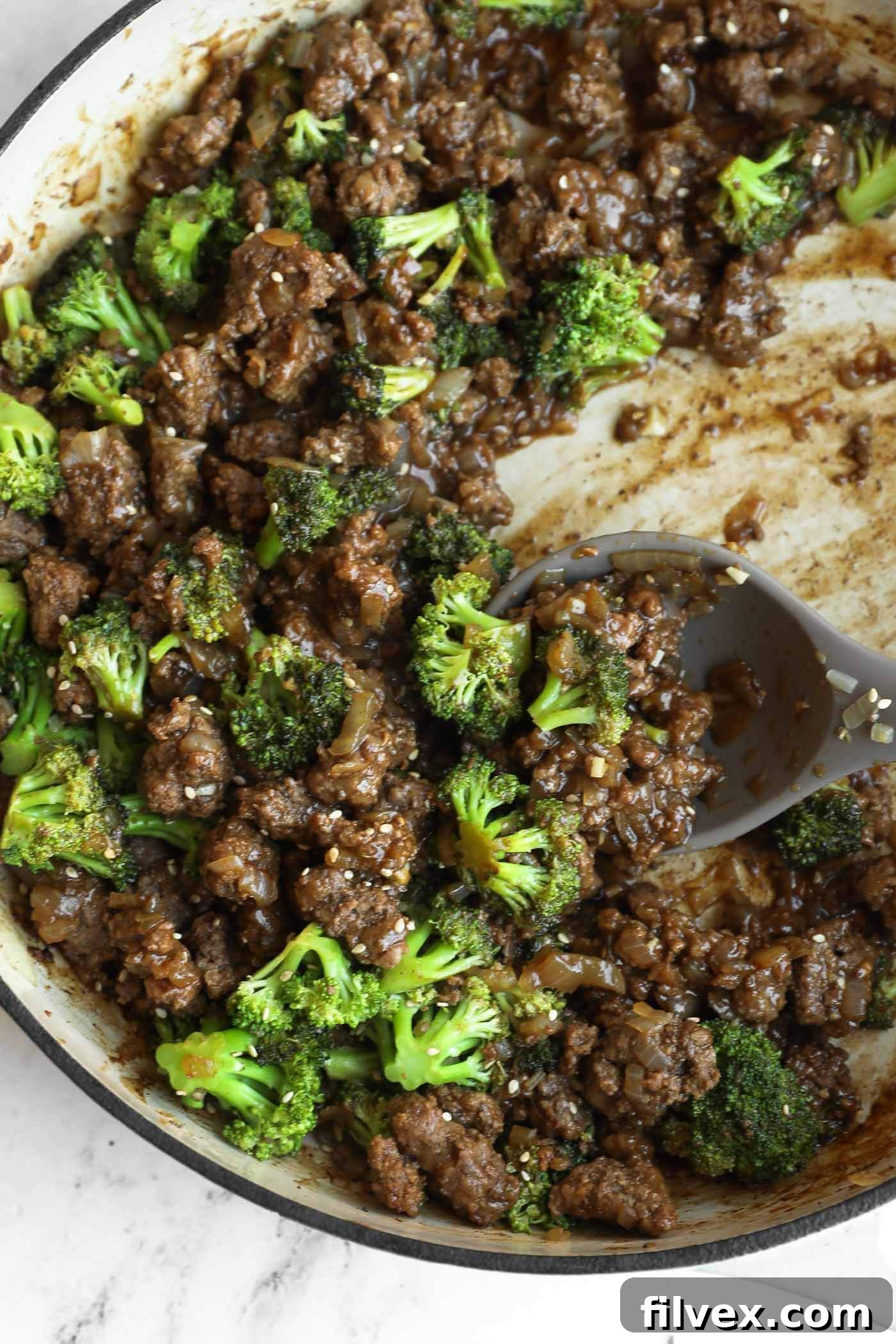 Ground beef, broccoli florets, and savory sauce come together in this easy one pan broccoli stir fry, all mixed in a large skillet with a serving spoon resting inside.