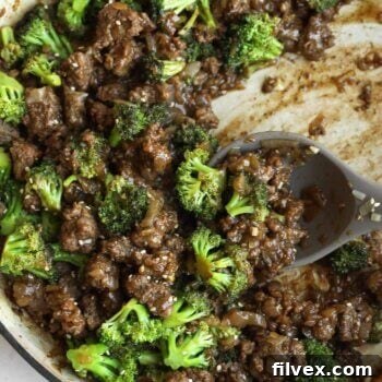 Ground beef, broccoli florets, and savory sauce come together in this easy one pan broccoli stir fry, all mixed in a large skillet with a serving spoon resting inside.