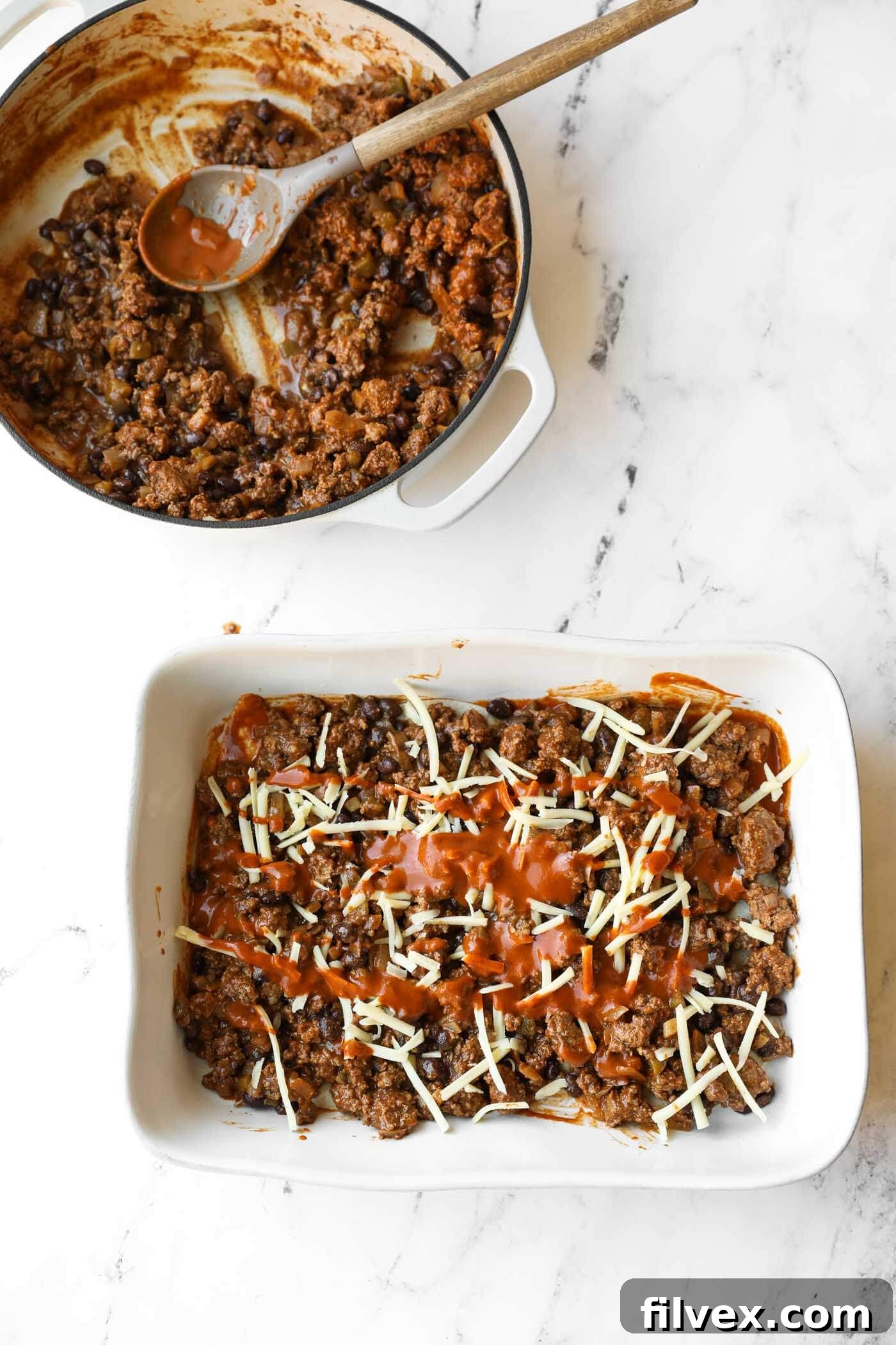 A baking dish filled with a ground meat and black bean mixture topped with shredded cheese and sauce sits next to a pot containing more of the mixture and a wooden spoon.